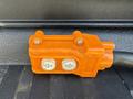 An orange electrical connector with two round buttons labeled with arrows