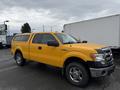 A yellow 2014 Ford F-150 with a silver grille and chrome wheels is parked, featuring a pickup truck design and a truck bed cover