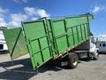 A 1997 Freightliner FL70 truck with a raised green dump bed, displaying large side panels and a back gate partially open