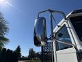 A shiny side mirror of a 2020 Peterbilt 330 truck reflecting surrounding trees and blue sky