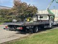 A 2022 Freightliner M2 106 tow truck with a flatbed and modern design parked on a driveway
