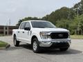 A 2021 Ford F-150 with a white exterior and chrome details facing forward parked on a paved surface