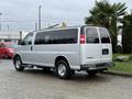 A silver 2021 Chevrolet Express van parked with its rear visible showcasing large windows and chrome wheels