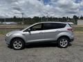 A silver 2015 Ford Escape parked on a gravel surface with visible side profile and four wheels