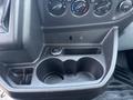 The interior of a 2016 Ford Transit 150 showcasing a console with climate control knobs and cup holders along with a 12V power outlet