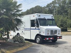 A white 2011 Workhorse W62 delivery truck with blue stripes parked on a lot with a distinctive boxy shape and large windshield