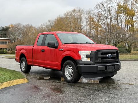 A red 2015 Ford F-150 pickup truck with a standard cab and black front grille parked on a wet surface