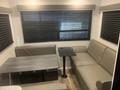 Interior of a 2022 Keystone Hide Out RDWE 20RDWE featuring a gray sofa and a small dining table with foldable seating