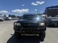 A 2010 Toyota Tacoma with a black exterior and a front bull bar is parked in a lot its hood has a scoop and the vehicle features off-road tires