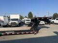 A 2020 Load Trail 28 foot gooseneck trailer with a flatbed design and black finish parked among several white trucks and vans