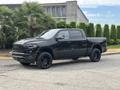 A black 2021 RAM 1500 pickup truck with a spacious cab and a bold front grille parked at an angle showcasing its stylish wheels and design