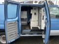 A blue 2009 Ford Econoline with doors open showing the interior space featuring metal shelving and a small refrigerator