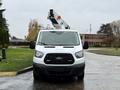 A 2019 Ford Transit van with a ladder rack on top is facing the viewer, featuring a white exterior and black accents.