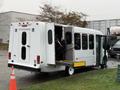 A white 2017 Ford E450 wheelchair accessible bus with a ramp extended for entry and multiple windows on the side