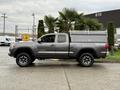 A 2016 Toyota Tacoma pickup truck in gray with a truck bed cover and off-road tires parked on a concrete surface