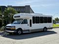 A white 2014 Chevrolet Express shuttle bus with large windows and a high roof is parked on a street