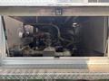 A 1999 Freightliner FL80 engine visible through an open compartment with various pipes and components connected to the engine