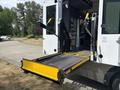 A wheelchair lift deployed from the back of a 2020 Chevrolet Express bus with yellow handrails and a textured metal platform