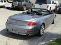 A silver 2004 BMW 6-Series convertible with a black interior and dual exhaust pipes is parked, showcasing its sleek design and sporty curves