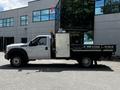 A 2016 Ford F-550 with a flatbed and tool storage compartment on the side parked beside a building