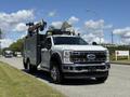 A 2023 Ford F-550 truck with a service body and equipment on top parked on a street