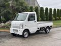 A white 2010 Suzuki Carry small truck with a flatbed and a compact design