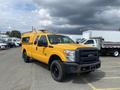 A bright yellow 2013 Ford F-250 SD truck with a black grille and roof racks parked at an outdoor location