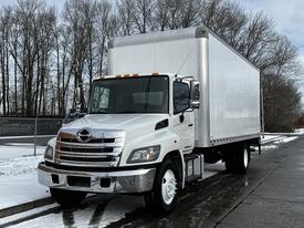 A 2019 Hino 338 24 foot cube truck with a white cargo box extended cab and chrome grille parked on a wet surface
