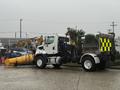 A white 2016 Freightliner 108SD truck with a yellow snow plow attached to the front and a reflective yellow and black tailgate