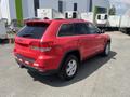 A red 2015 Jeep Grand Cherokee parked with a clear view of its rear and side highlighting its sleek design and larger tires