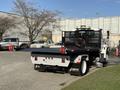 A 2017 International 4300 tow truck with a flatbed featuring a black mesh back and two red winches on the sides parked on a lot