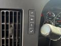 The dashboard of a 2020 Chevrolet Express featuring control buttons for lights, door, and a checklist symbol with a round air vent and speedometer in the background