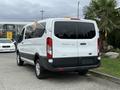 A white 2017 Ford Transit T150 XLT van parked with a flag attached on the rear and a large rear window