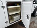 A white service truck door is open revealing a storage compartment with two batteries on the bottom shelf and empty space above them