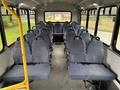 Interior of a 2018 Chevrolet Express featuring rows of grey upholstered seats arranged in a spacious layout with a yellow pole near the entrance