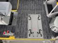 The interior floor of a 2009 Toyota Hiace featuring a grey patterned carpet with two seatbelt anchors and a flat area with four brackets for securing wheelchairs or equipment