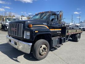 A black and orange 1996 GMC Top Kick flatbed truck facing slightly to the right with a large, chrome front bumper and a visible ladder on the side