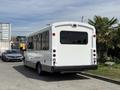 A white 2017 Chevrolet Express bus with windows on the sides and back parked in a lot with a simple rear design and no visible branding
