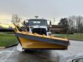 A white 2016 Freightliner 108SD snow plow truck is positioned in front with a large yellow snow plow attachment attached to the front
