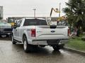 A silver 2015 Ford F-150 truck parked with its tailgate down showing the 4x4 logo and the Ford emblem on the back