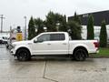 A 2018 Ford F-150 in white with black rims parked on a wet surface
