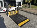 A yellow and black wheelchair lift is partially lowered from the back of a 2017 Ford Transit-350 vehicle