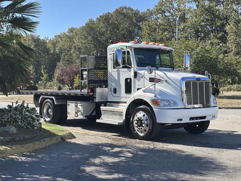 A 2020 Peterbilt 330 truck with a flatbed design featuring a white exterior and chrome accents parked with a clear view of its front and side