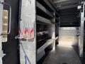 Interior of a 2023 Mercedes-Benz Sprinter 2500 featuring metal shelving units and straps mounted on the side for securing cargo