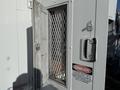 A 2011 Freightliner M2 106 with a side door partially opened revealing a metal grate and a sign warning of danger inside the compartment