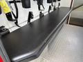 A black cushioned bench with safety straps attached to a wall in a vehicle interior