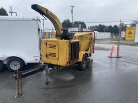 A yellow 2010 Vermeer Corporation BC1000XL wood chipper with a feeding chute an attached tow hitch and large wheels for mobility