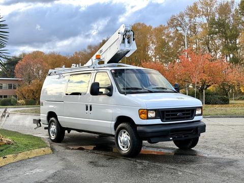 A 2007 Ford Econoline van with a raised utility ladder on top parked on a road