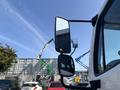 A 2014 Freightliner M2 106 truck with side mirrors reflecting a blue sky and construction equipment in the background