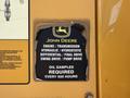 A weathered label on a John Deere 710K machine detailing engine transmission and maintenance requirements including oil samples every 500 hours